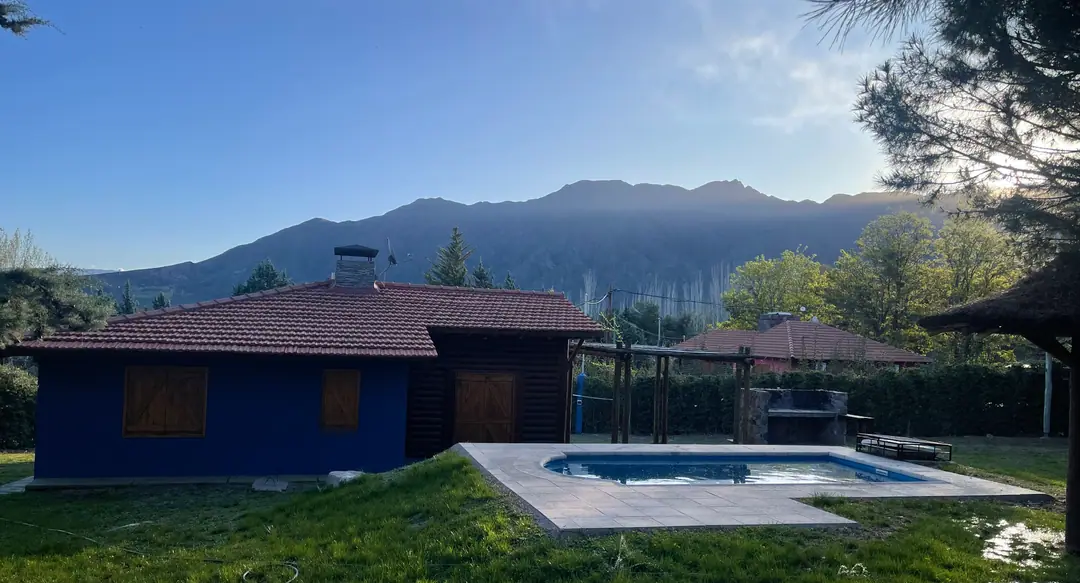 Cabaña Malbec, de troncos y pintada de azul, con su piscina y la cordillera de Los Andes detrás