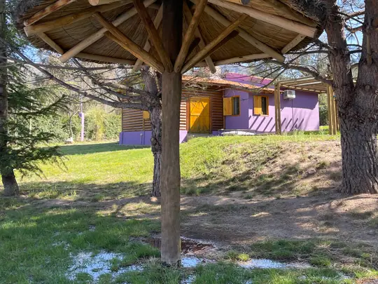 Sombrilla de paja y troncos en el parque, con la cabaña Borgoña detrás