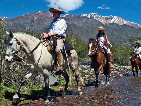 Cabalgata cruzando un arroyo con la cordillera detrás