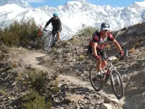 Ciclistas de montaña bajando por un sendero con cerros nevados