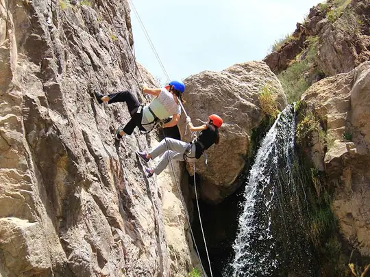 Personas haciendo rappel en una pared de roca junto a una cascada