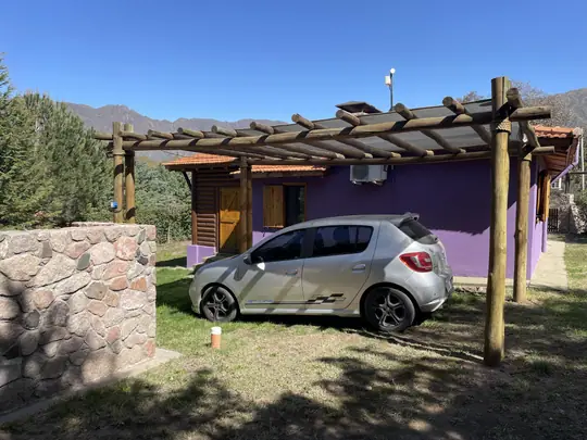 Auto estacionado bajo la pérgola junto a la cabaña