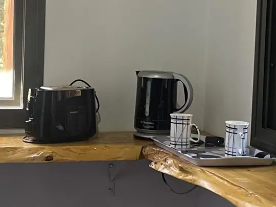 Tostadora, pava eléctrica y tazas sobre una barra de madera